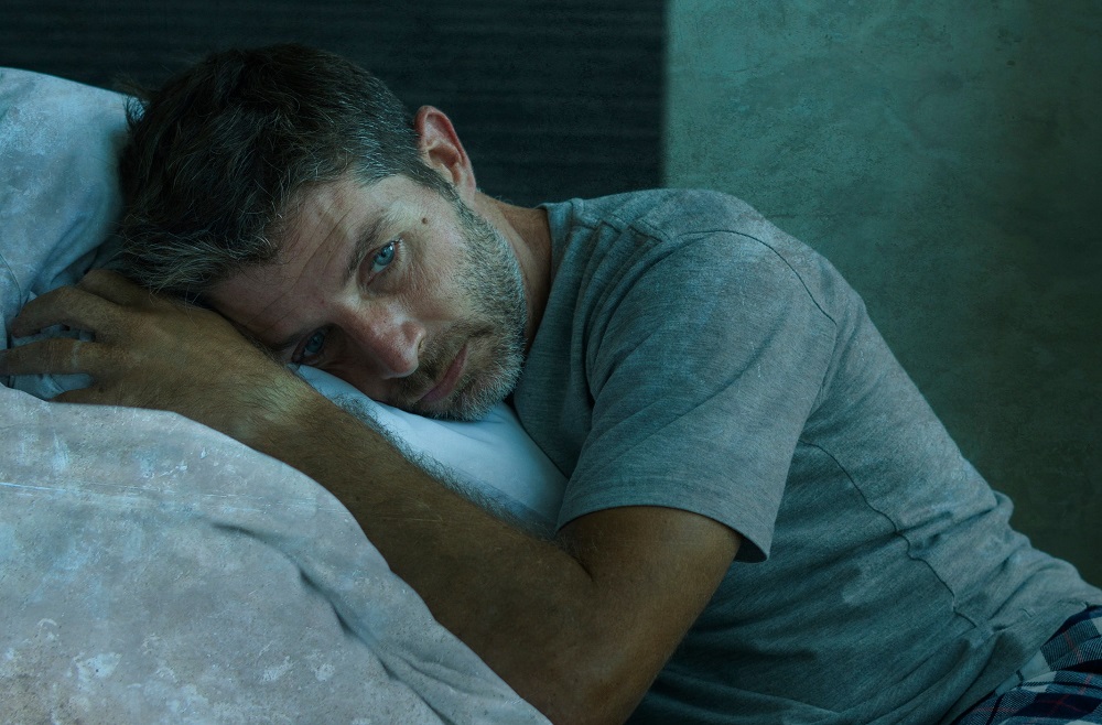 Portret dramatic al unui bărbat de 40 de ani. Este speriat și deprimat, stând pe pat, îmbrăcat în pijamale.