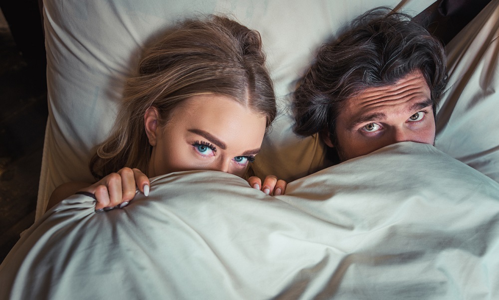 Parteneri timizi care au parte de intimitate, stau în pat și își acoperă fața.
