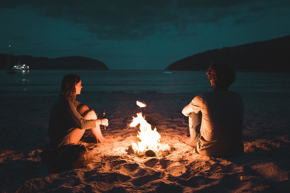 Cuplu care stă pe plajă și se încălzește la foc