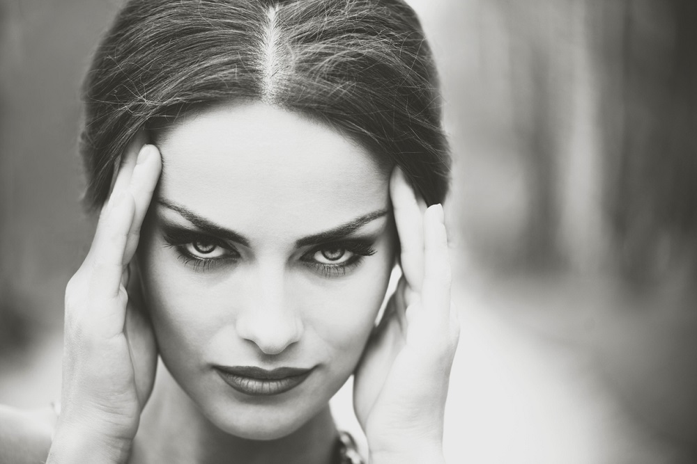 Brunetă frumoasă cu privire pătrunzătoare, ținându-se cu mâinile de tâmple.
