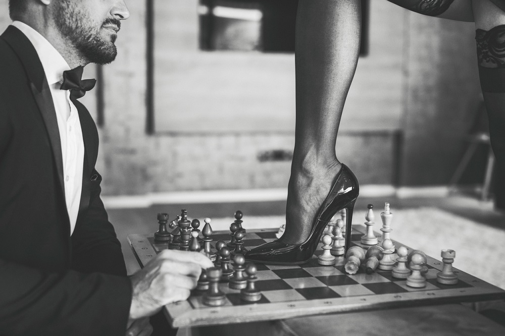 Femeie care poartă tocuri, urcată pe tabla de șah a partenerului.
