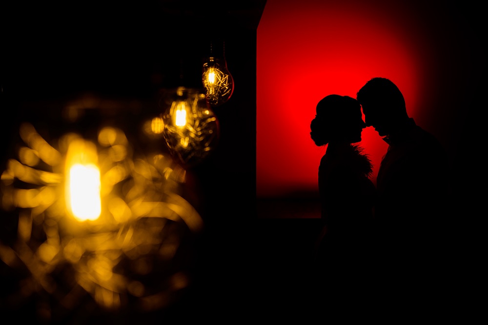 Siluetele unor parteneri îmbrățișați, stând împreună într-o lumină roșie difuză.