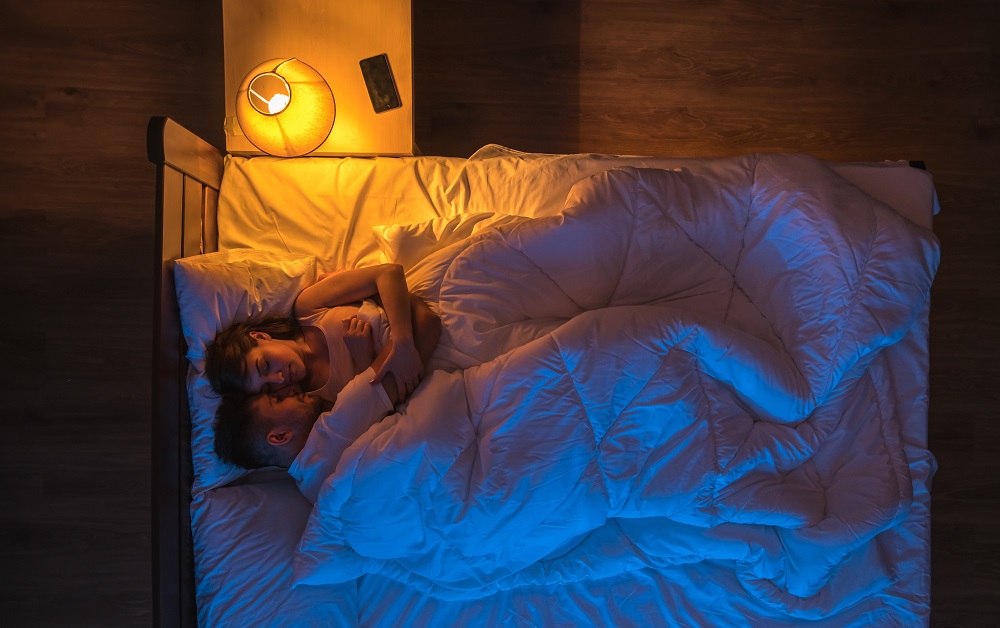 Parteneri care dorm îmbrățișați în intimitatea dormitorului lor.