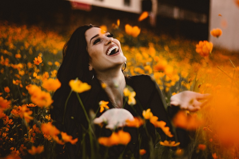 Femeie fericită care se bucură de natură, fotografie realizată pe un câmp plin cu flori.