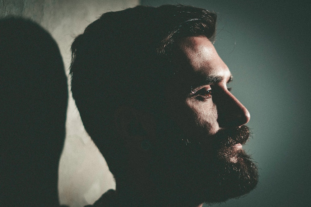 Imagine din profil a unui bărbat cu barbă care stă serios și privește în față.