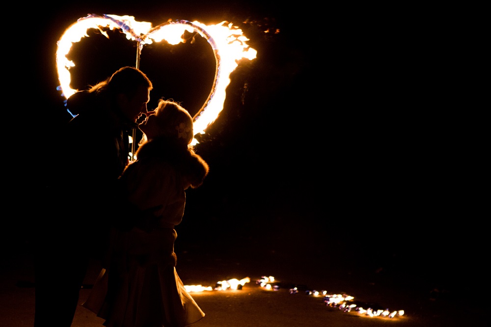 Cuplu care se sărută pasional în fața unei inimi de foc