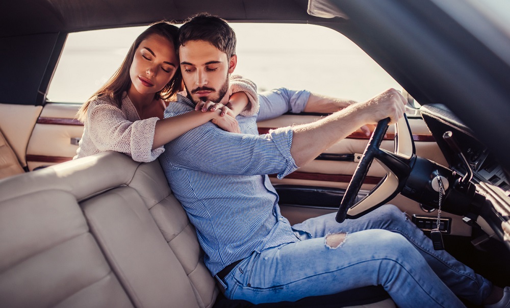 Femeie îndrăgostită care își îmbrățișează partenerul aflat la volanul unei mașini.