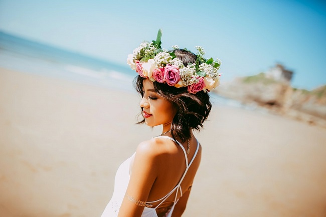 Mireasă pe plajă care are pe cap o coroană din flori.