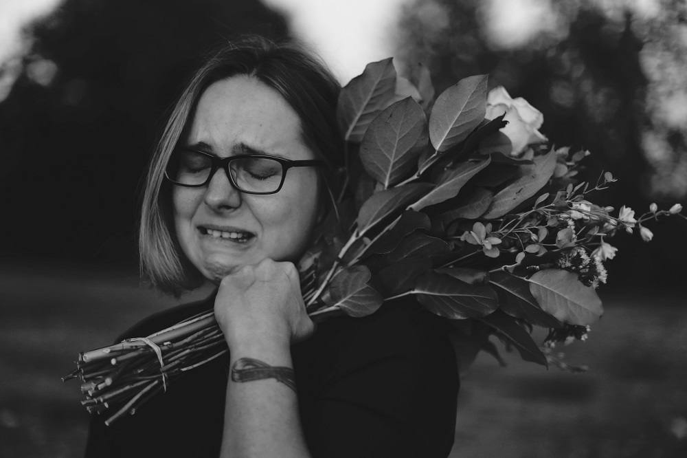 Femeie îndoliată care plânge cu un buchet de flori în mână.