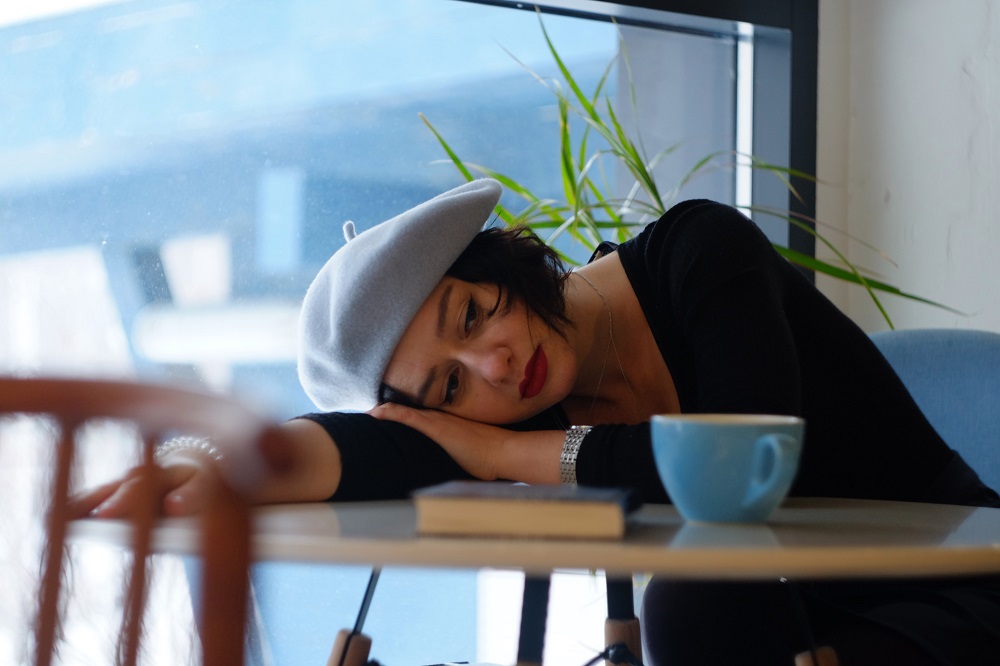 Femeie supărată și anxioasă, stând cu capul pe masă, în timp ce bea o cafea.