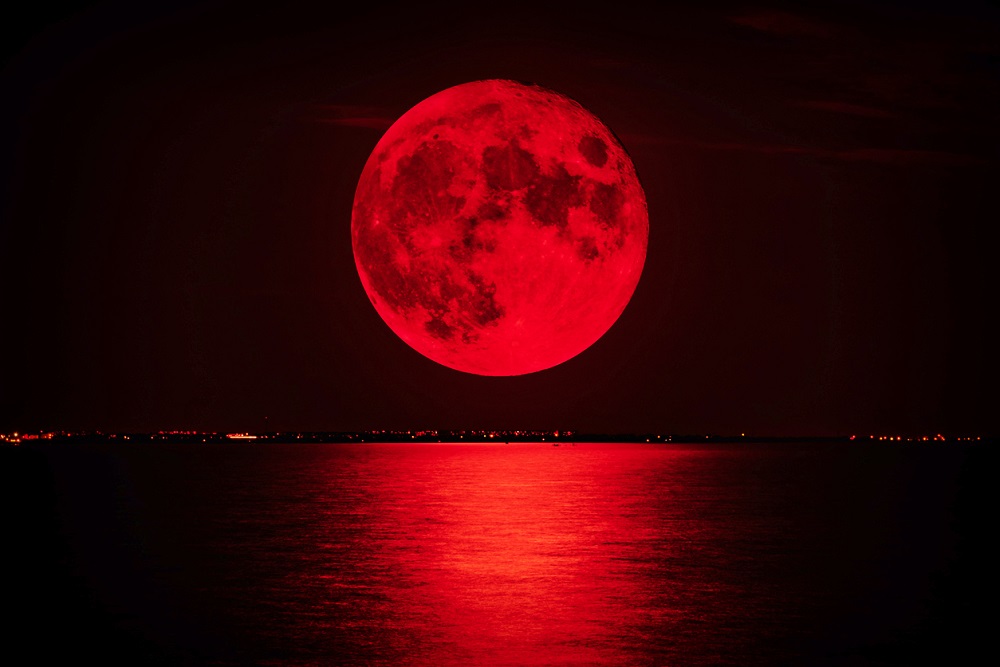 Peisaj nocturn în nuanțe de roșu, în care lacul este luminat de Luna Plină.