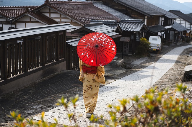 Imagine din Japonia cu o femeie îmbrăcată în kimono, care se plimbă cu o umbrelă de soare deasupra capului.