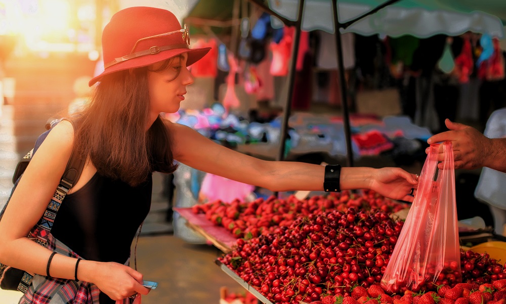 Femeie cu pălărie roșie care cumpără cireșe din piață.