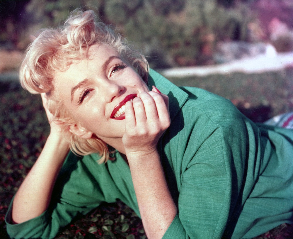 Actrița Marilyn Monroe pozează pentru un portret întinsă pe iarbă, în 1954, în Palm Springs, California