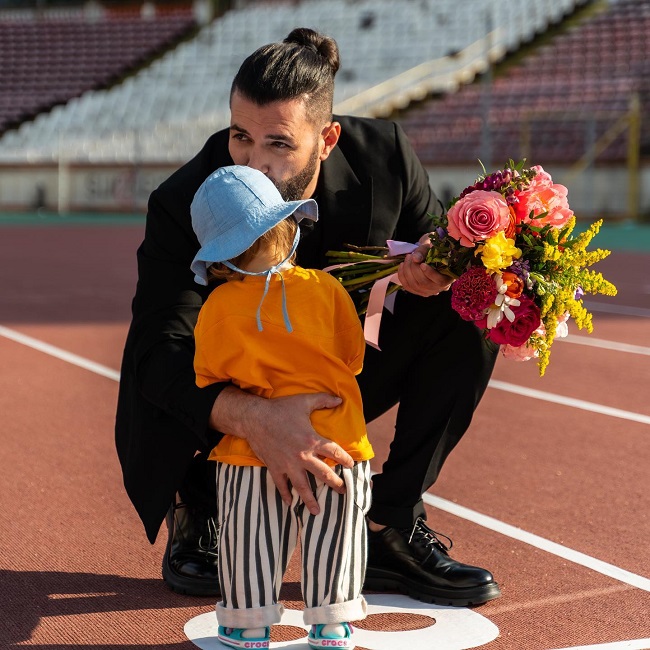 Smiley își sărută fiica pe cap, în timp ce ține un buchet de flori în mână.