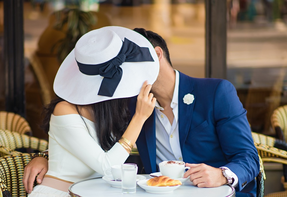 Parteneri care se sărută sub o pălărie la masa unei cafenele din Paris.