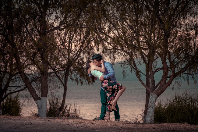 Parteneri care să sărută pasional pe malul unui lac, printre copaci.