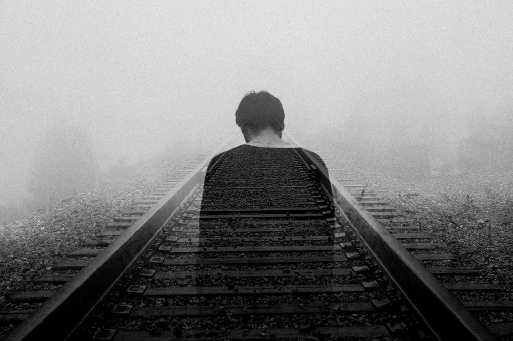 Ilustrație a conceptului de singurătate - persoană anxioasă care stă singură pe șinele de tren.