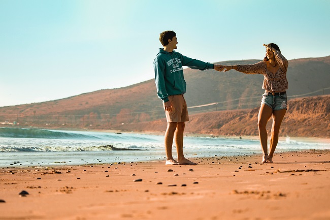 Îndrăgostiți care se plimbă de mână pe plajă.