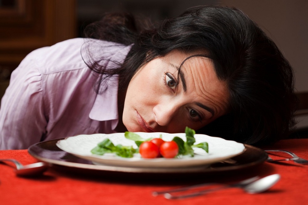Femeie care se uită contrariată la mâncarea de dietă din farfurie.