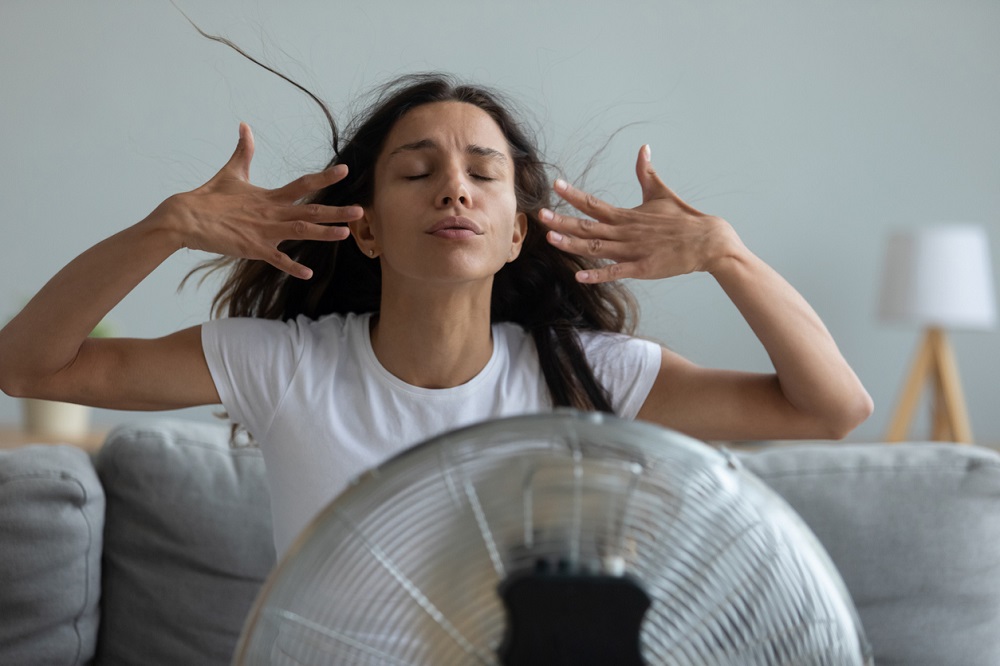 Femeie care stă lângă un ventilator, încercând să se răcorească.