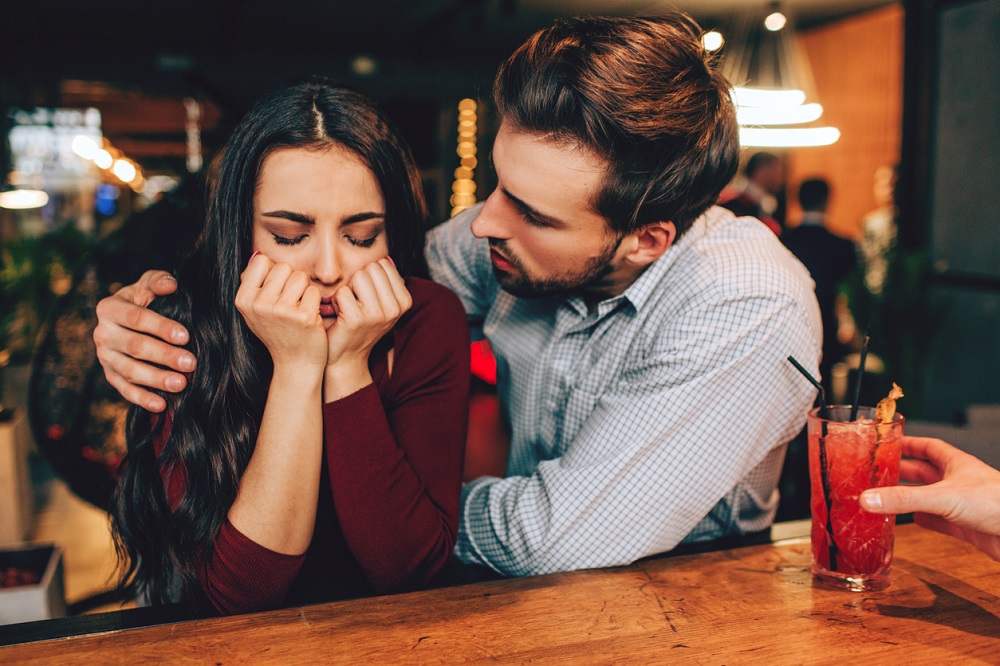 Bărbat care consolează o femeie tristă într-un bar.