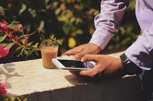 Bărbat care se uită în telefon, în timp ce își bea cafeaua.