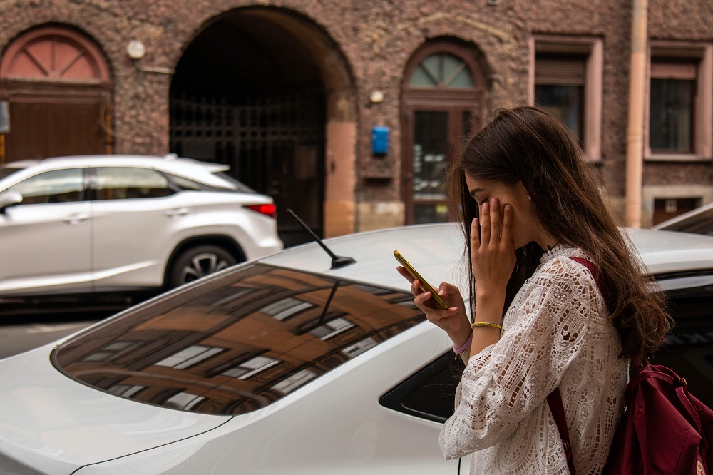 Femeie în bluză albă care își verifică telefonul pe stradă.