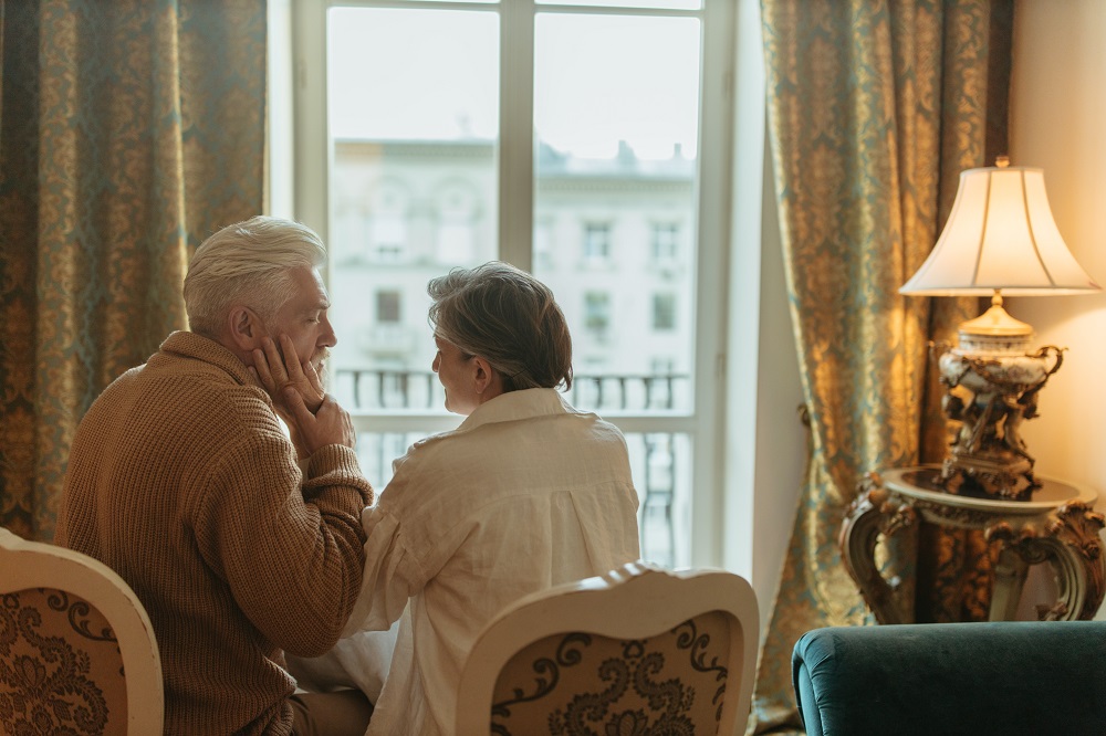 Parteneri în vârstă care stau pe scaun, în timp ce femeia mângâie fața bărbatului.