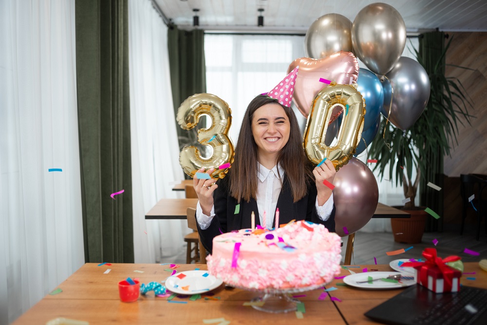 Femeie fericită la aniversarea ei de 30 de ani, înconjurată de confetti, baloane, cadouri și tort