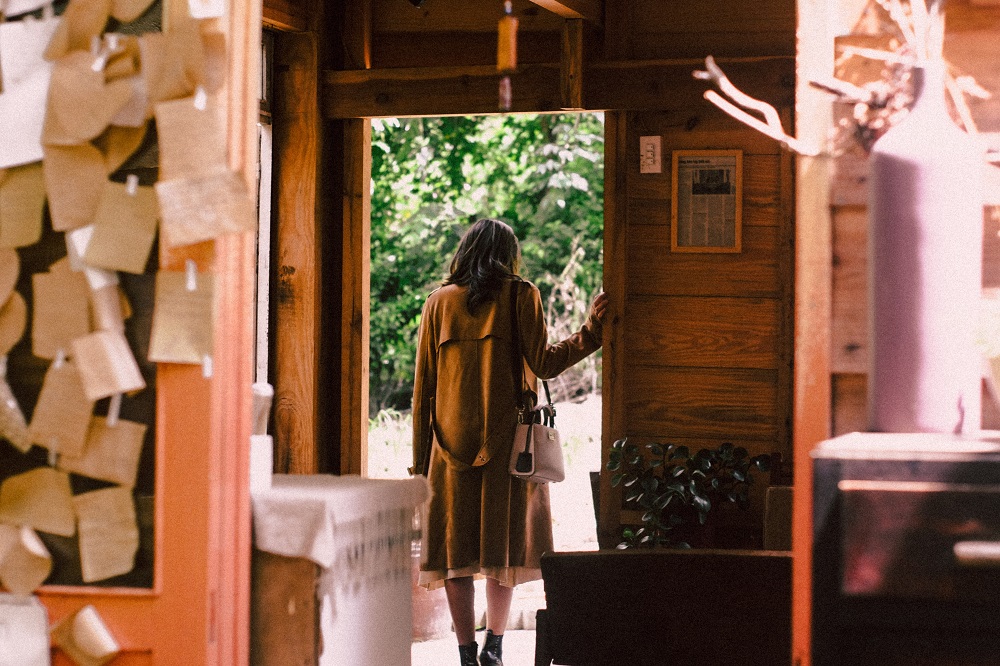 Femeie îmbrăcată în maro, în timp ce iese pe ușa unei cabane.
