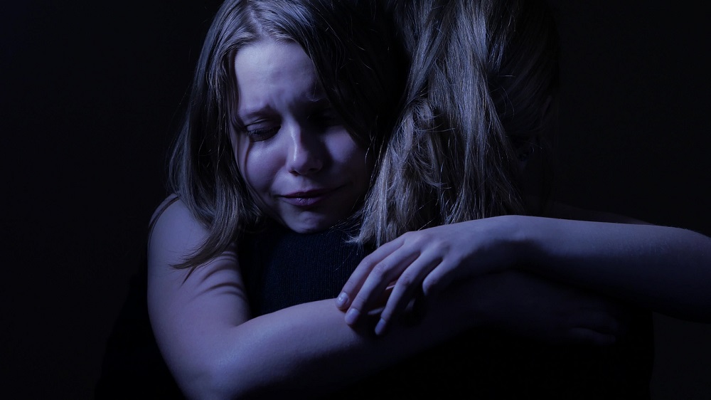 Tânără care plânge în timp ce își îmbrățișează strâns mama.