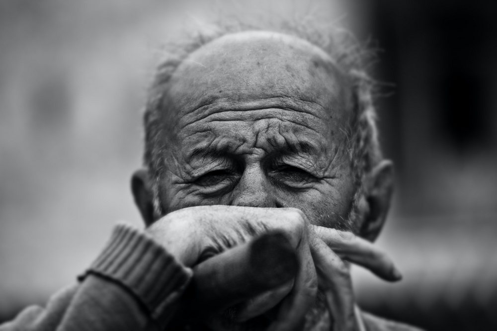 Bătrân care plânge și își ține mâna la nas.