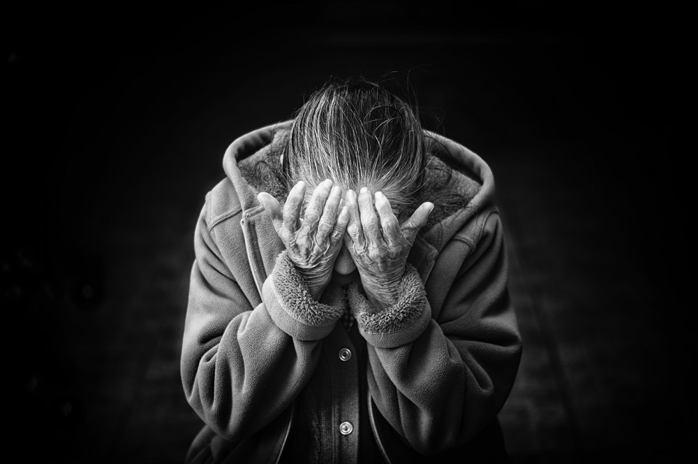 Femeie în vârstă care plânge și își acoperă fața cu mâinile.