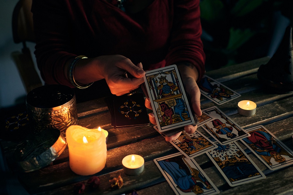 Persoană care ghicește în cărțile de tarot așezate pe masă, alături de alte elemente care țin de magie.
