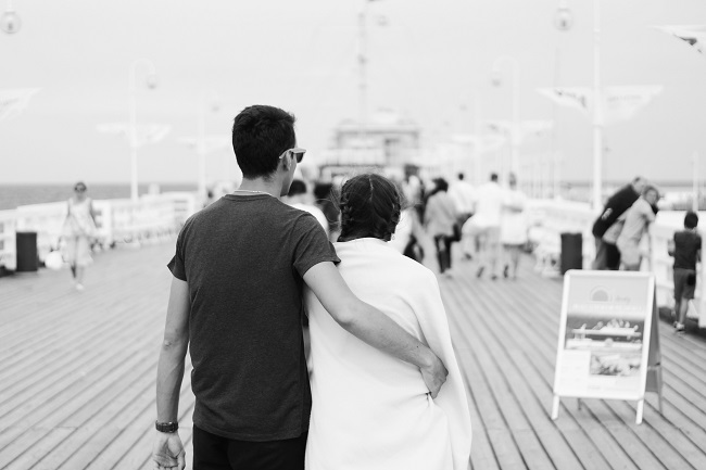 Imagine alb-negru cu un cuplu îmbrățișat care se plimbă pe un ponton.
