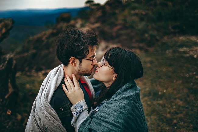 Parteneri care se sărută într-un peisaj montan, acoperiți cu pături groase.