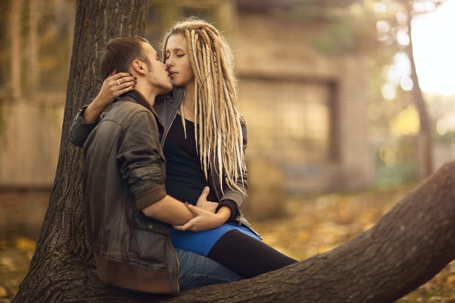 Cuplu care se îmbrățișează și se sărută, stând pe o creangă.