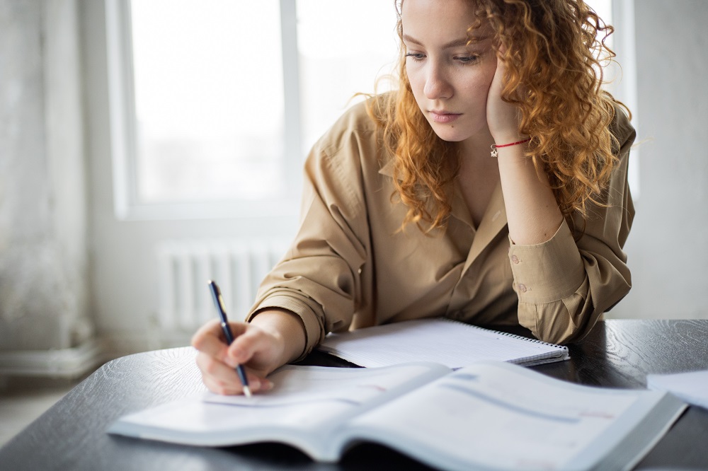 Femeie blondă și creață care stă la birou și studiază