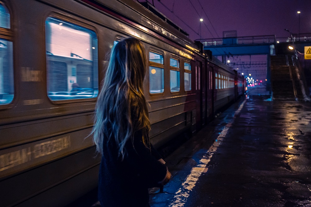 Femeie tristă care privește cum pleacă trenul din gară.