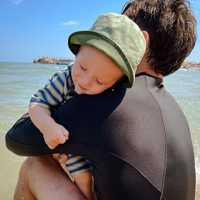Dani Oțil, ținându-și fiul în brațe pe malul mării.