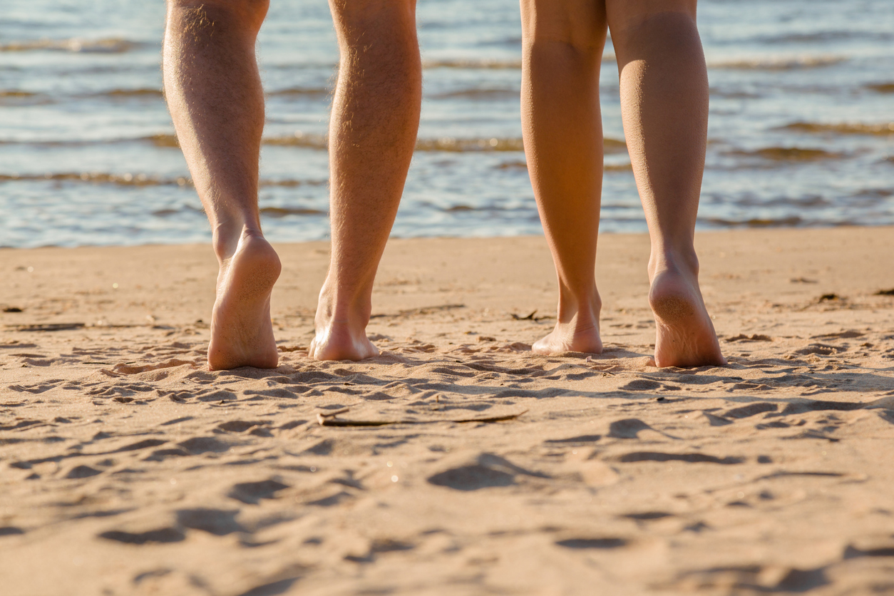 Picioarele unor parteneri care se plimbă pe plajă, cu tălpile goale pe nisip.
