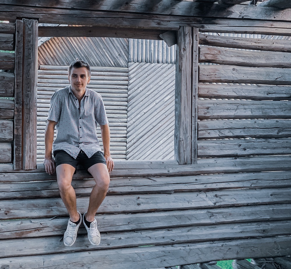 Bărbat în cămașă care stă pe pervazul unei clădiri din lemn