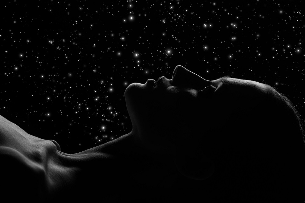 Femeie întinsă pe spate care privește cerul plin cu stele.
