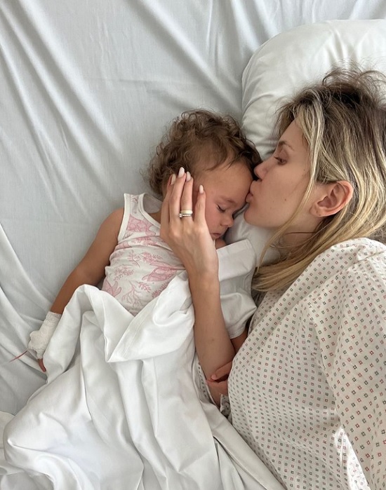 Emily Burghelea își sărută fiica pe frunte, în timp ce împart amândouă un pat de spital.