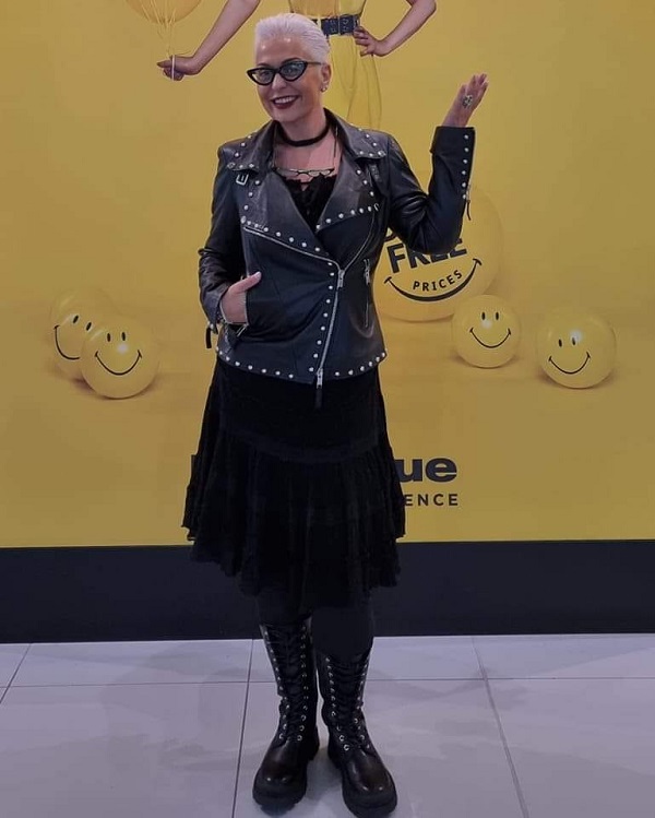 Monica Anghel zâmbitoare, îmbrăcată într-o rochie neagră pe care a accesorizat-o cu o geacă de piele și cu o pereche de cizme tot din piele