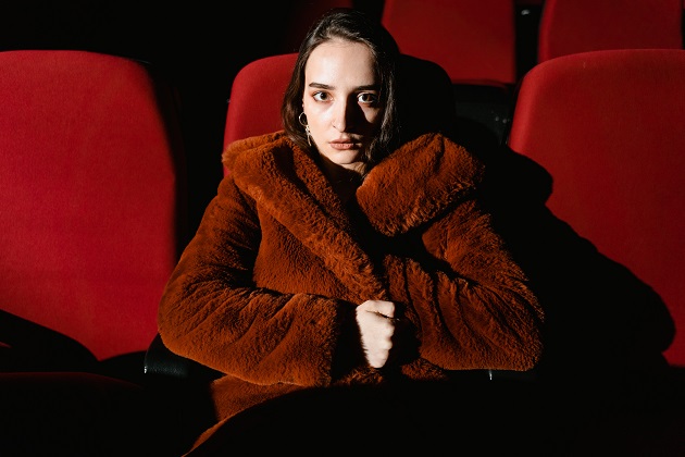 Femeie bogată care poartă o haină roșie din blană, în timp ce stă într-o sală de teatru.