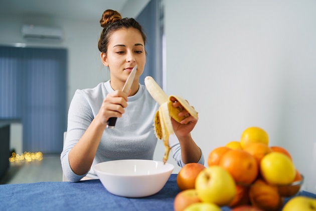 Femeie care stă pe scaun în bucătărie, în timp ce decojește și taie o banană coaptă