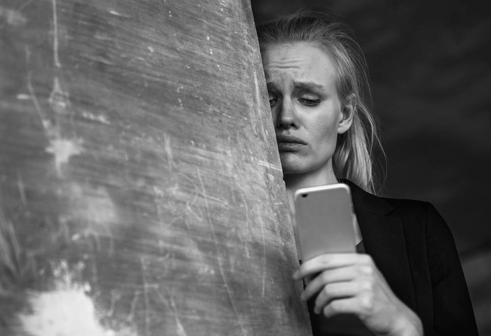 Femeie care stă sprijinită de un stâlp în timp ce se uită dezamăgită la un mesaj primit pe telefon.