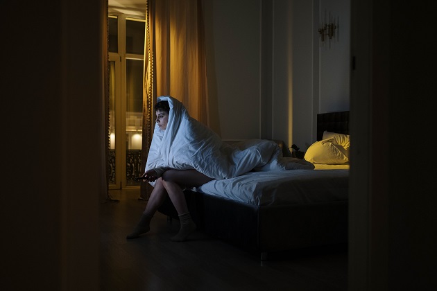 Femeie care stă pe pat, în întuneric și cu plapuma pe ea